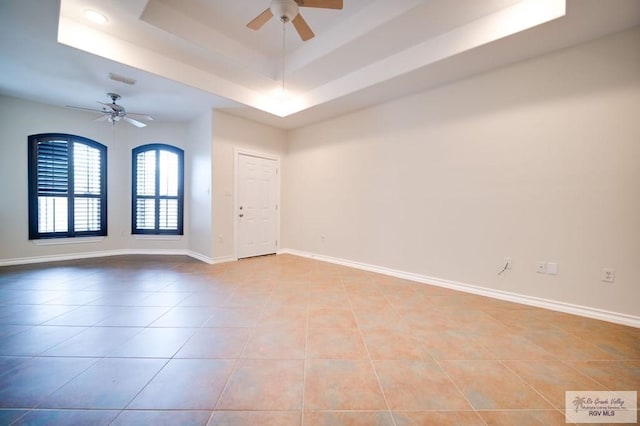 tiled empty room featuring a tray ceiling and ceiling fan