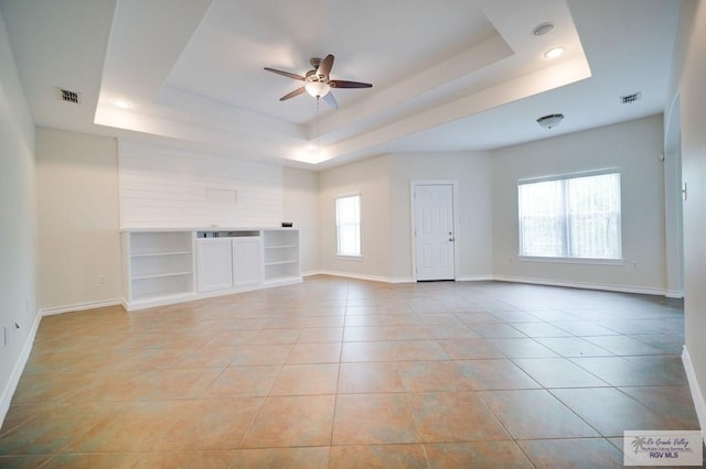 unfurnished living room featuring a raised ceiling, ceiling fan, built in features, and light tile patterned floors