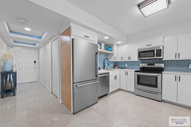 kitchen featuring white cabinetry, stainless steel appliances, a tray ceiling, and sink