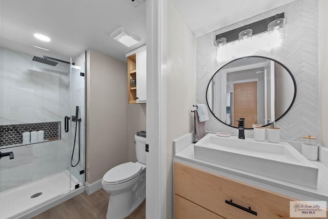 bathroom featuring hardwood / wood-style flooring, vanity, a shower with shower door, and toilet