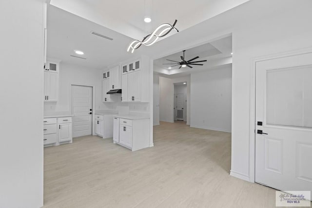 kitchen with ceiling fan, a tray ceiling, light hardwood / wood-style flooring, and white cabinets