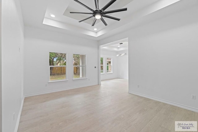 empty room with a raised ceiling, ceiling fan, and light hardwood / wood-style flooring