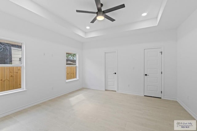 spare room with light hardwood / wood-style flooring, ceiling fan, and a tray ceiling