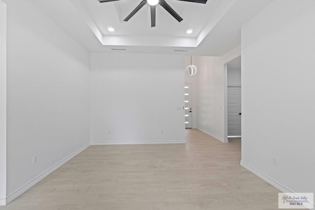 empty room featuring ceiling fan, a tray ceiling, and light hardwood / wood-style floors