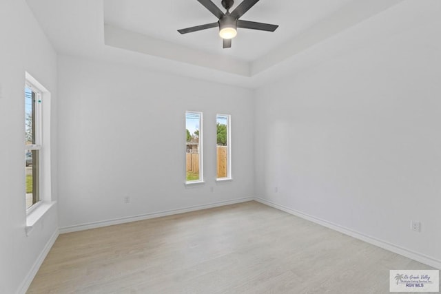 empty room with light hardwood / wood-style flooring, ceiling fan, and a tray ceiling