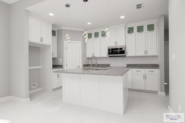 kitchen featuring white cabinetry, sink, hanging light fixtures, light stone counters, and an island with sink