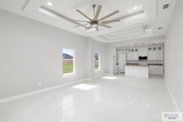 unfurnished living room featuring ceiling fan, sink, and a tray ceiling