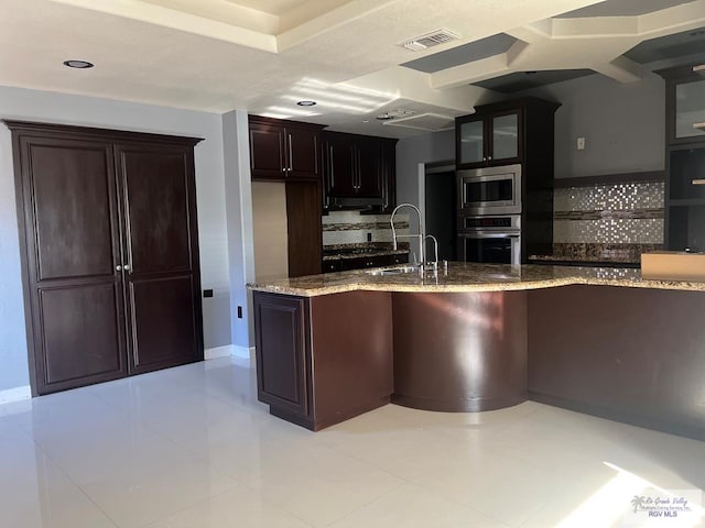 kitchen featuring light stone counters, dark brown cabinetry, stainless steel appliances, and tasteful backsplash