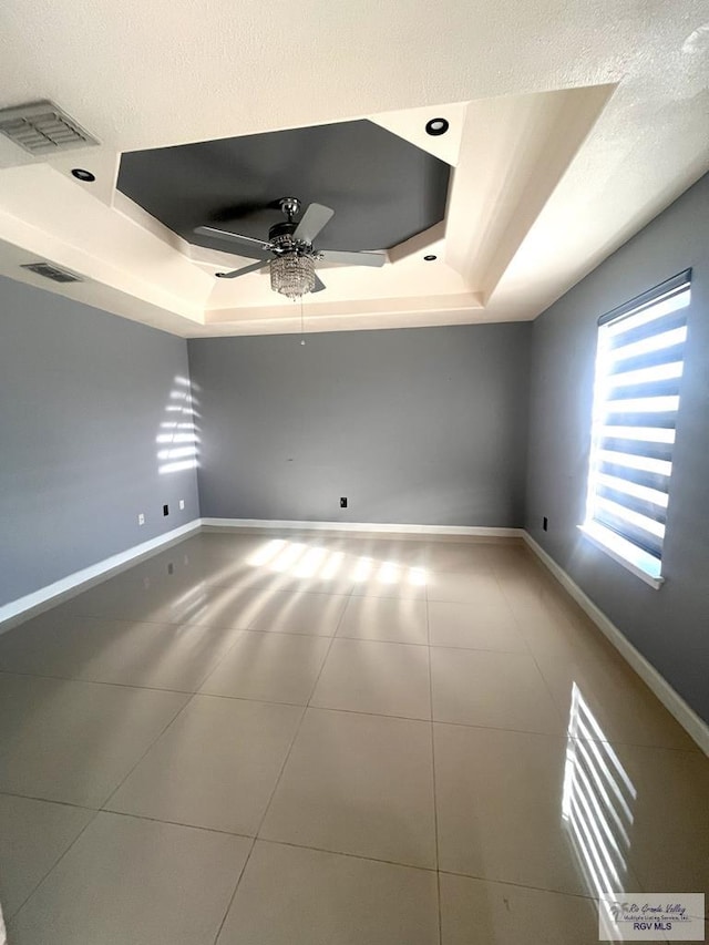 spare room featuring a raised ceiling, ceiling fan, tile patterned floors, and a textured ceiling