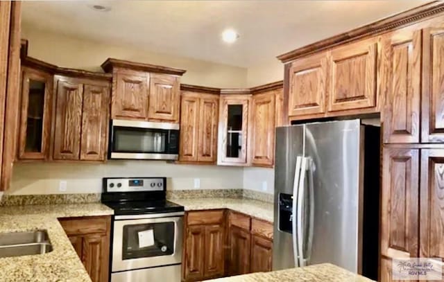 401 S Tamm Ln, Harlingen, TX 78550 - kitchen featuring appliances with stainless steel finishes, glass insert cabinets, light stone counters, and brown cabinetry