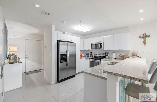 kitchen featuring sink, appliances with stainless steel finishes, a kitchen breakfast bar, white cabinets, and kitchen peninsula