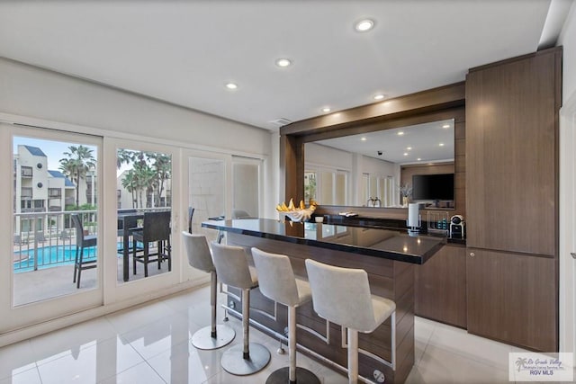 kitchen featuring light tile patterned floors, dark brown cabinets, a breakfast bar area, and a center island