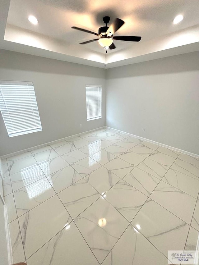 empty room featuring a raised ceiling and ceiling fan