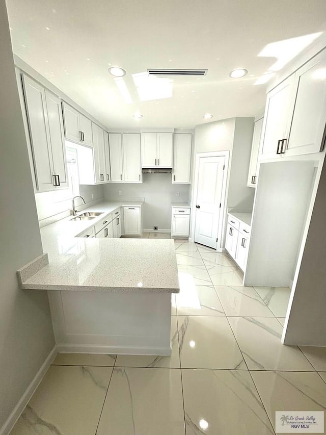 kitchen featuring light stone counters, sink, kitchen peninsula, and white cabinets