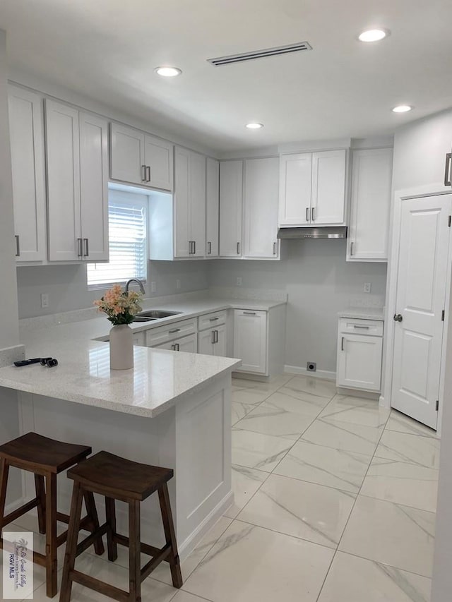 kitchen with white cabinetry, sink, kitchen peninsula, and a kitchen bar