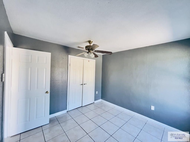 unfurnished bedroom with light tile patterned floors, a closet, and ceiling fan