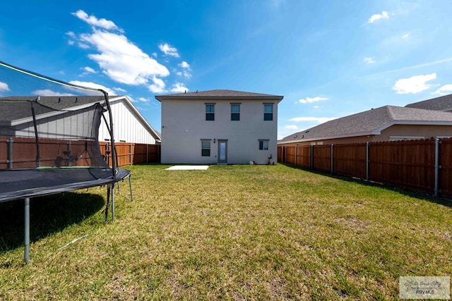 back of house with stucco siding, a fenced backyard, a trampoline, and a yard