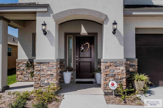 doorway to property with a garage, stone siding, and stucco siding