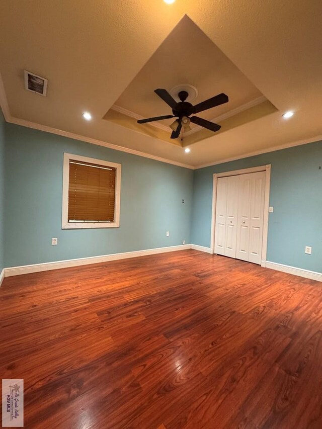 unfurnished bedroom featuring hardwood / wood-style floors, ceiling fan, ornamental molding, and a tray ceiling