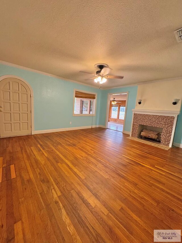 unfurnished living room featuring ornamental molding, a textured ceiling, ceiling fan, a tile fireplace, and light hardwood / wood-style floors