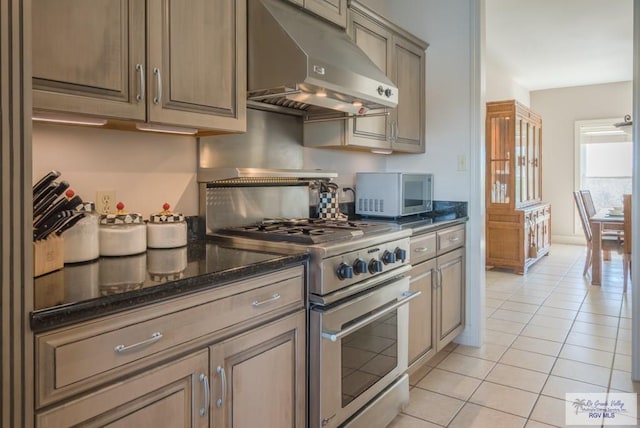 kitchen with under cabinet range hood, light tile patterned floors, stainless steel range, and dark stone countertops