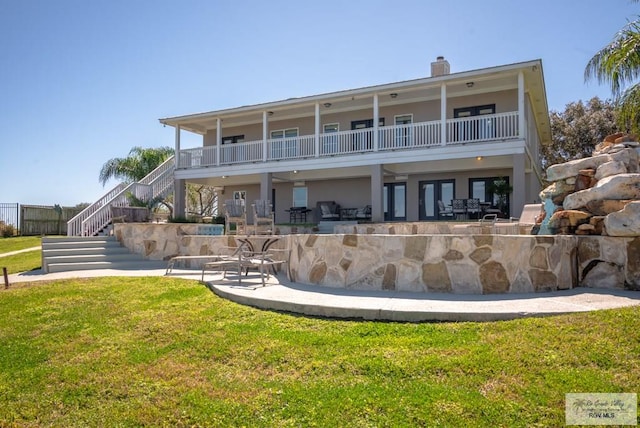 rear view of house featuring a lawn, a patio, a balcony, a chimney, and stairs