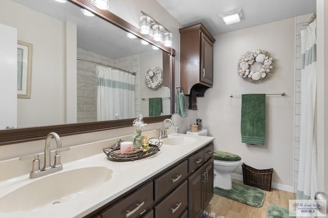 bathroom with a sink, double vanity, toilet, and wood finished floors