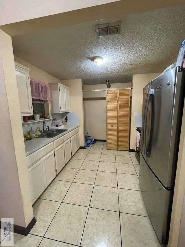 kitchen featuring white cabinets, light tile patterned floors, stainless steel fridge, and a textured ceiling