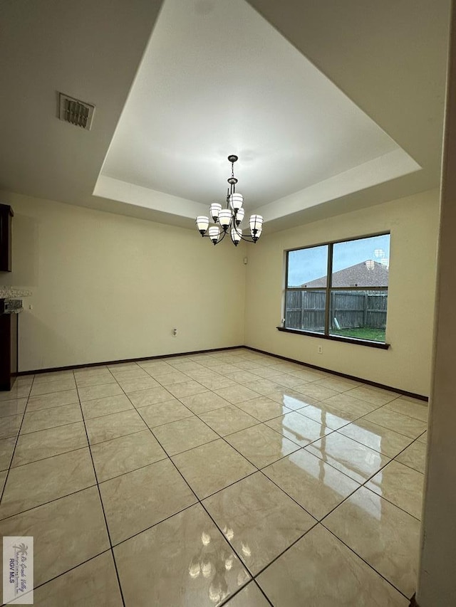 empty room with a raised ceiling, light tile patterned floors, and an inviting chandelier