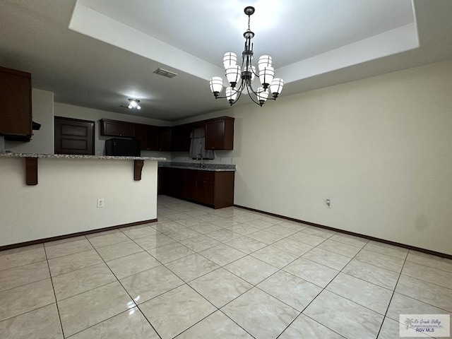 kitchen featuring black refrigerator, a tray ceiling, a notable chandelier, kitchen peninsula, and light stone countertops