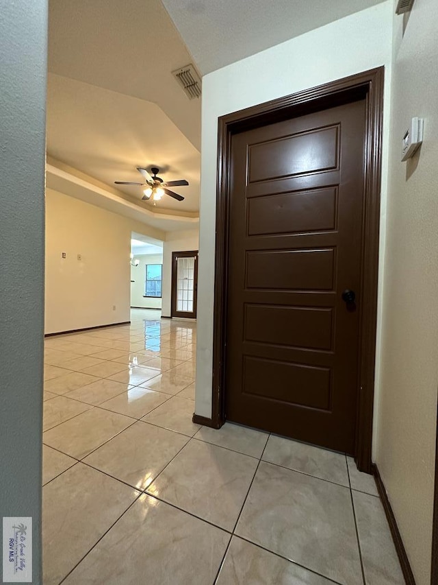 corridor featuring a tray ceiling and light tile patterned floors