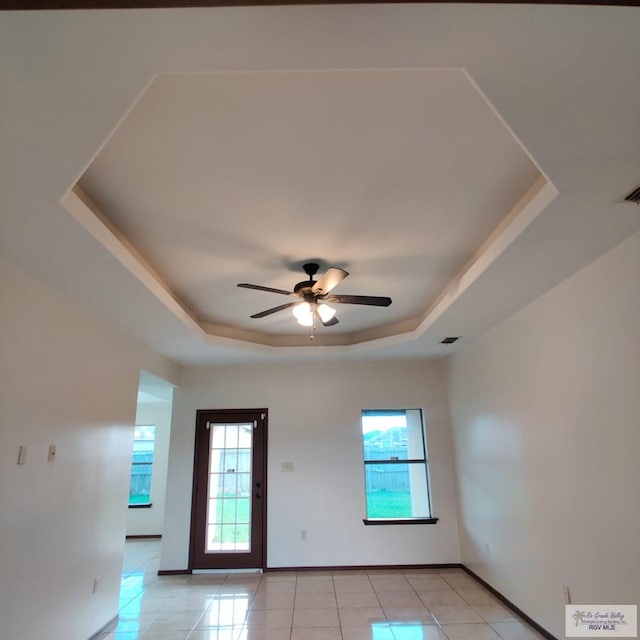 tiled spare room with ceiling fan, a raised ceiling, and a wealth of natural light