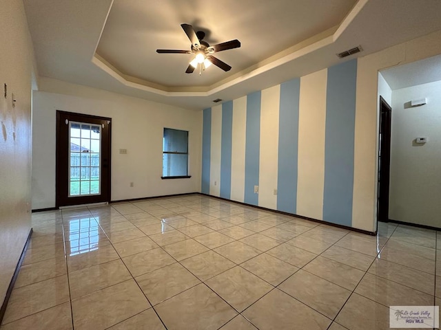 tiled empty room with ceiling fan and a raised ceiling