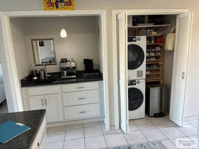 clothes washing area with light tile patterned flooring, stacked washer / dryer, and sink