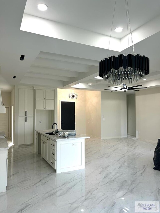 kitchen with a kitchen island with sink, a tray ceiling, white cabinets, ceiling fan, and sink