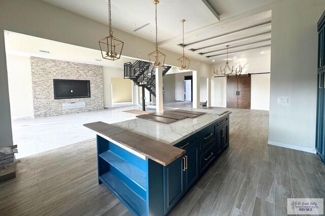 kitchen featuring light stone counters, blue cabinets, dark wood-type flooring, decorative light fixtures, and a center island