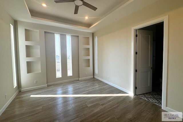 unfurnished room with a raised ceiling, built in features, and hardwood / wood-style floors