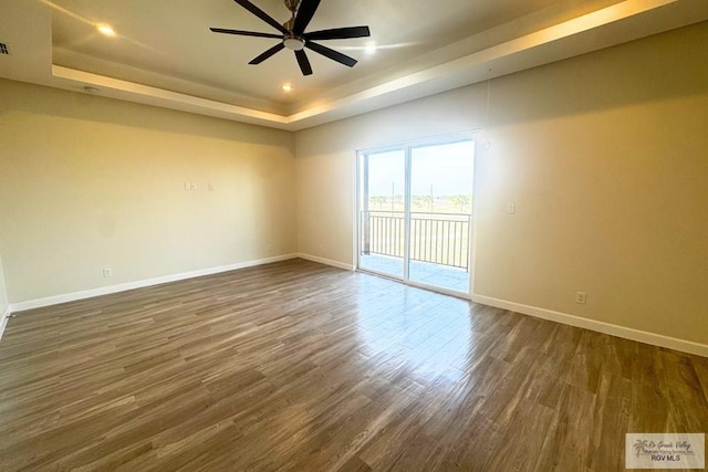 unfurnished room with a raised ceiling, ceiling fan, and dark wood-type flooring