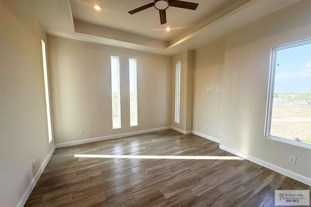 spare room with a raised ceiling, ceiling fan, and dark hardwood / wood-style flooring