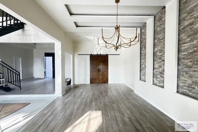 unfurnished dining area featuring a barn door, an inviting chandelier, and hardwood / wood-style flooring