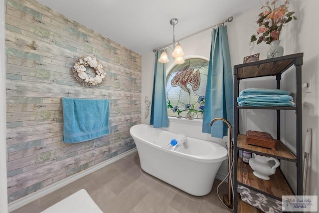 full bathroom with wooden walls, an accent wall, baseboards, an inviting chandelier, and a freestanding tub