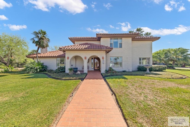 mediterranean / spanish house featuring brick siding, a front yard, and a tiled roof