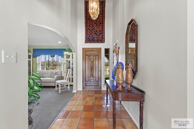 carpeted foyer with tile patterned floors, a notable chandelier, arched walkways, a high ceiling, and baseboards