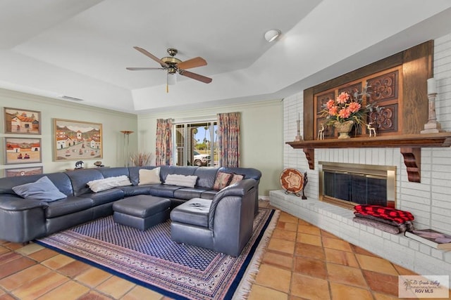 living room featuring a ceiling fan, visible vents, a raised ceiling, a brick fireplace, and tile patterned floors