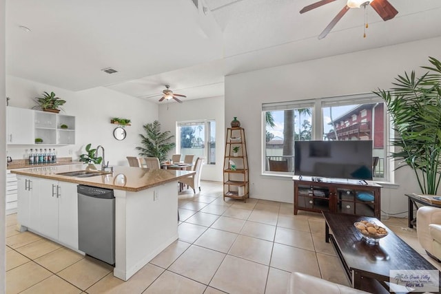 kitchen with stainless steel dishwasher, a kitchen island with sink, sink, white cabinets, and light tile patterned flooring