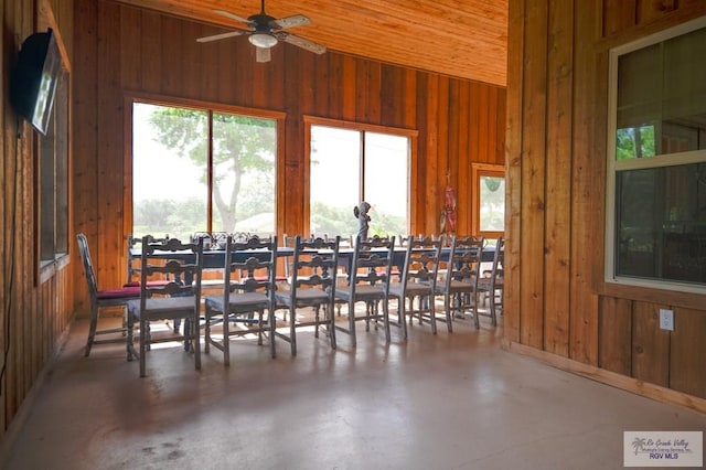 dining area with wooden walls, high vaulted ceiling, and concrete flooring