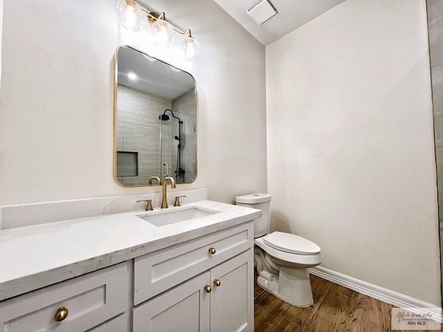 bathroom with baseboards, toilet, wood finished floors, walk in shower, and vanity