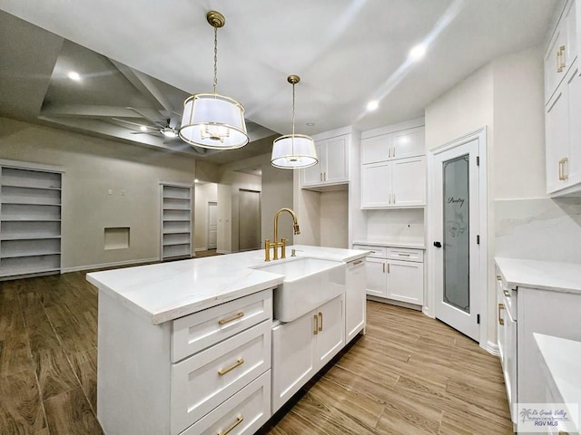 kitchen featuring decorative light fixtures, white cabinets, a sink, and wood finished floors