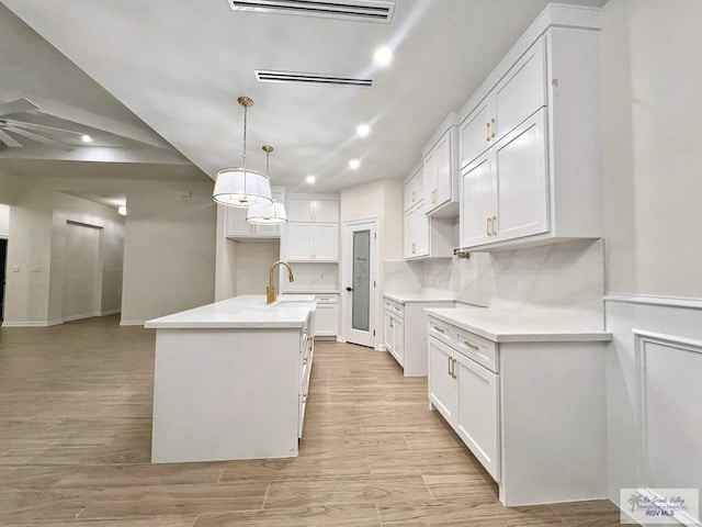 kitchen featuring a center island with sink, white cabinets, a sink, ceiling fan, and light wood-type flooring