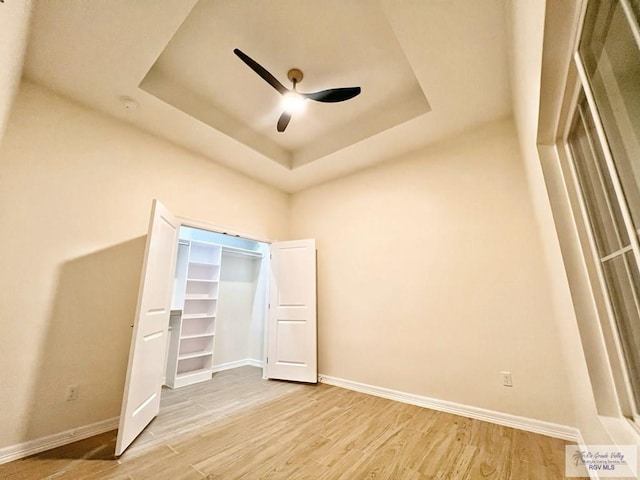 unfurnished bedroom featuring light wood-type flooring, baseboards, and a tray ceiling